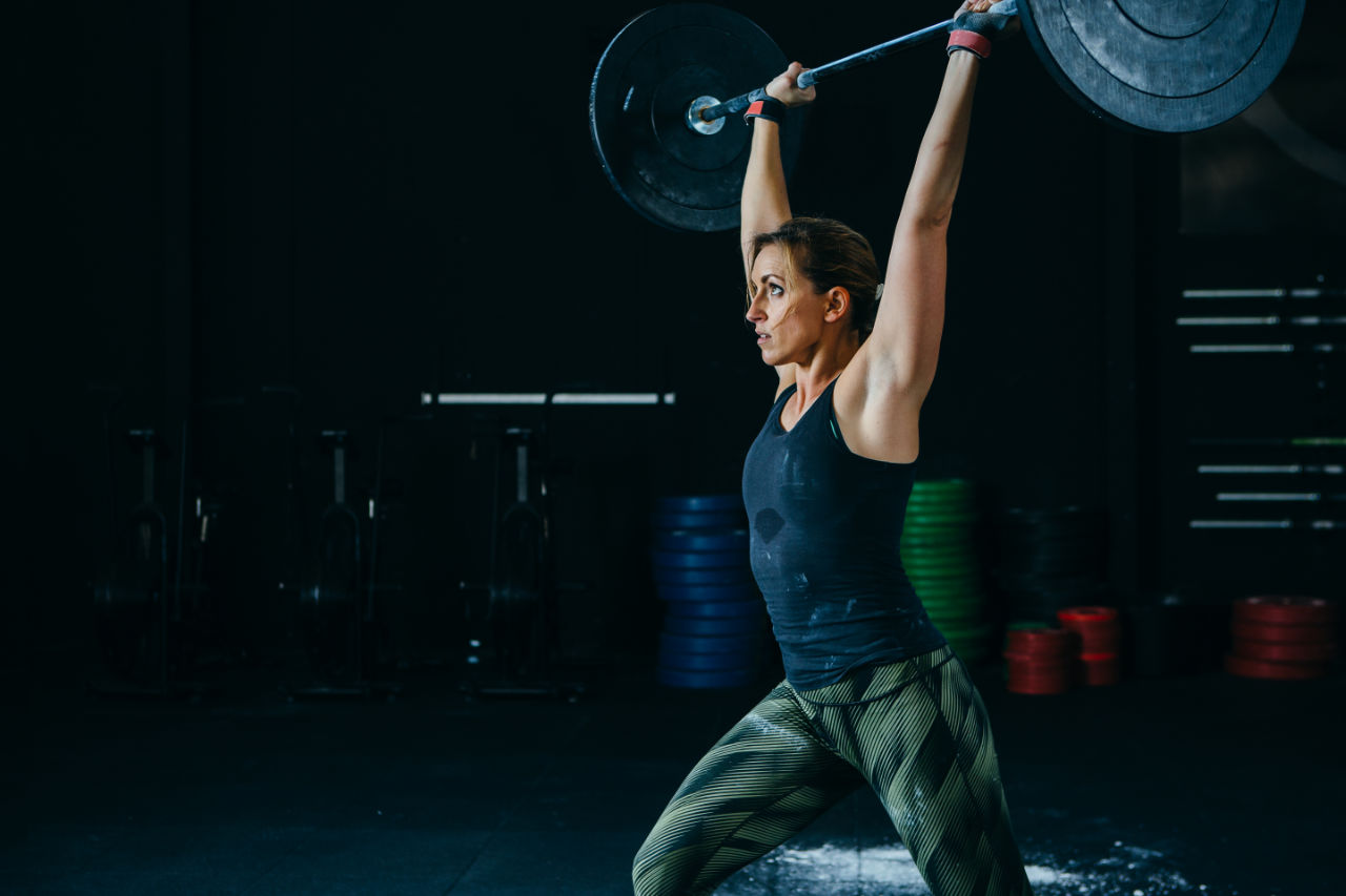 Young sporty woman does jerks with barbell at box gym on a fitness routine.